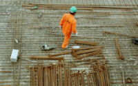 A construction worker in a green hardhat and an orange jumpsuit on the worksite.